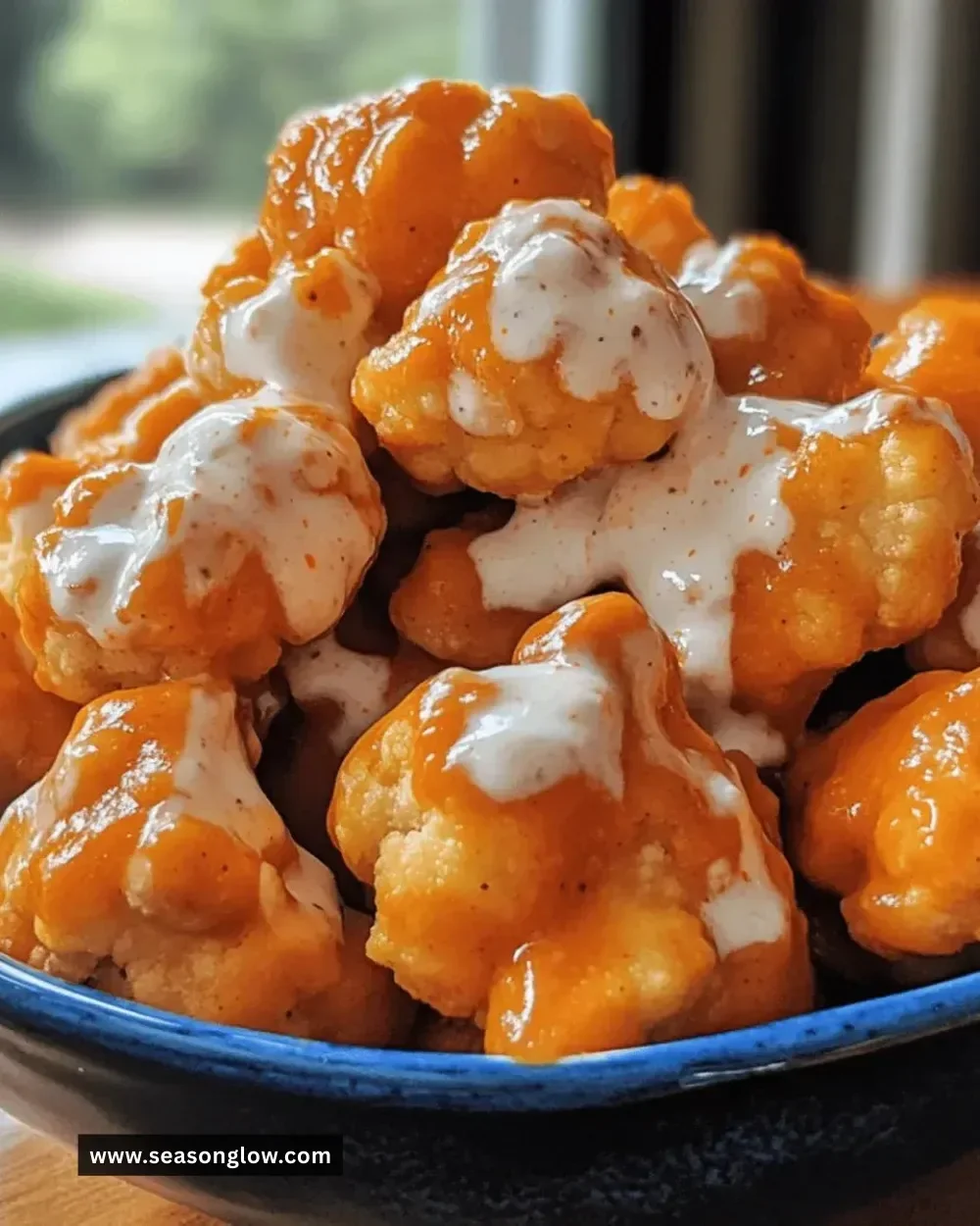 Crispy Buffalo Cauliflower bites drizzled with creamy sauce on a plate.
