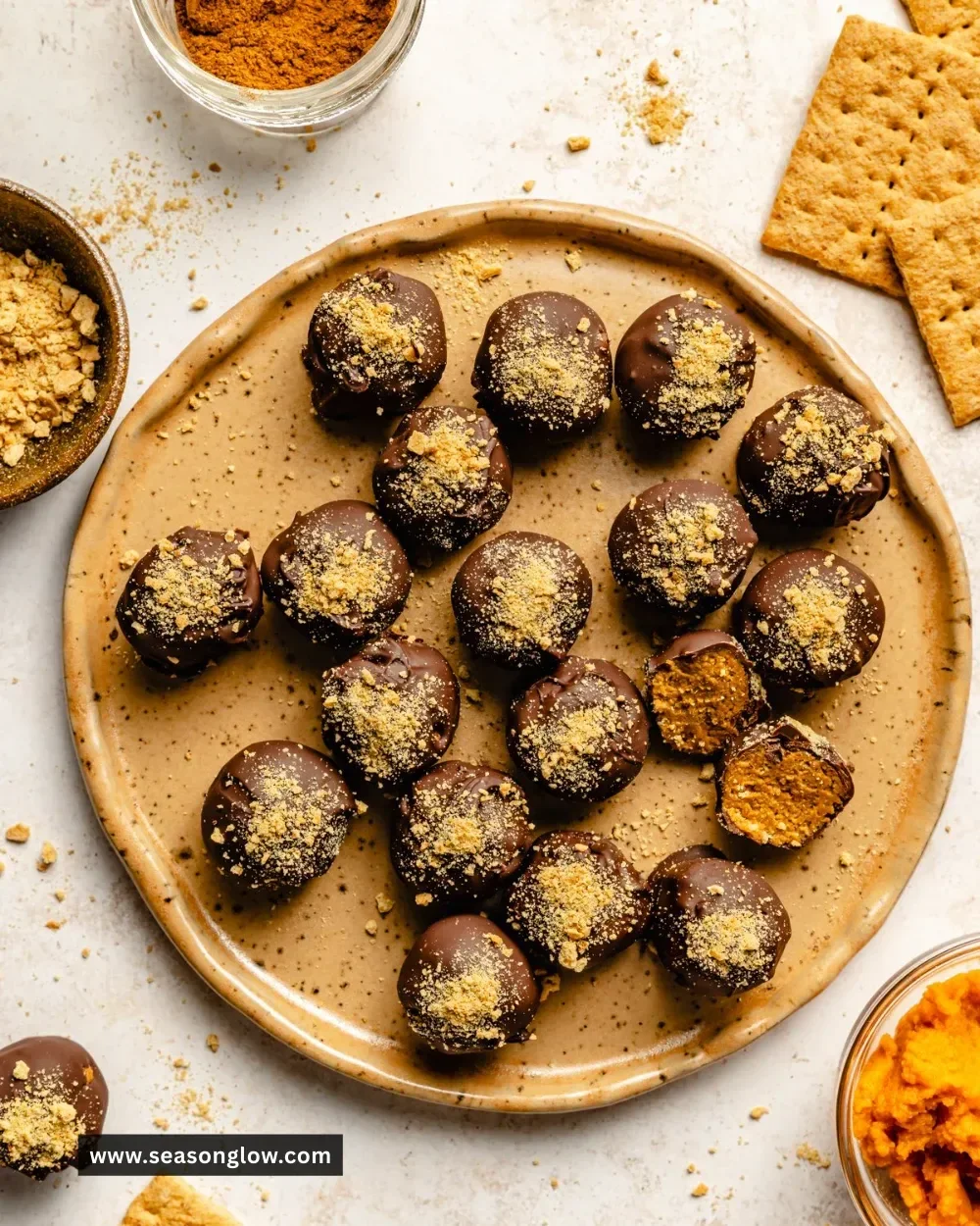 Delicious no-bake pumpkin truffles on a white plate decorated with autumn leaves.