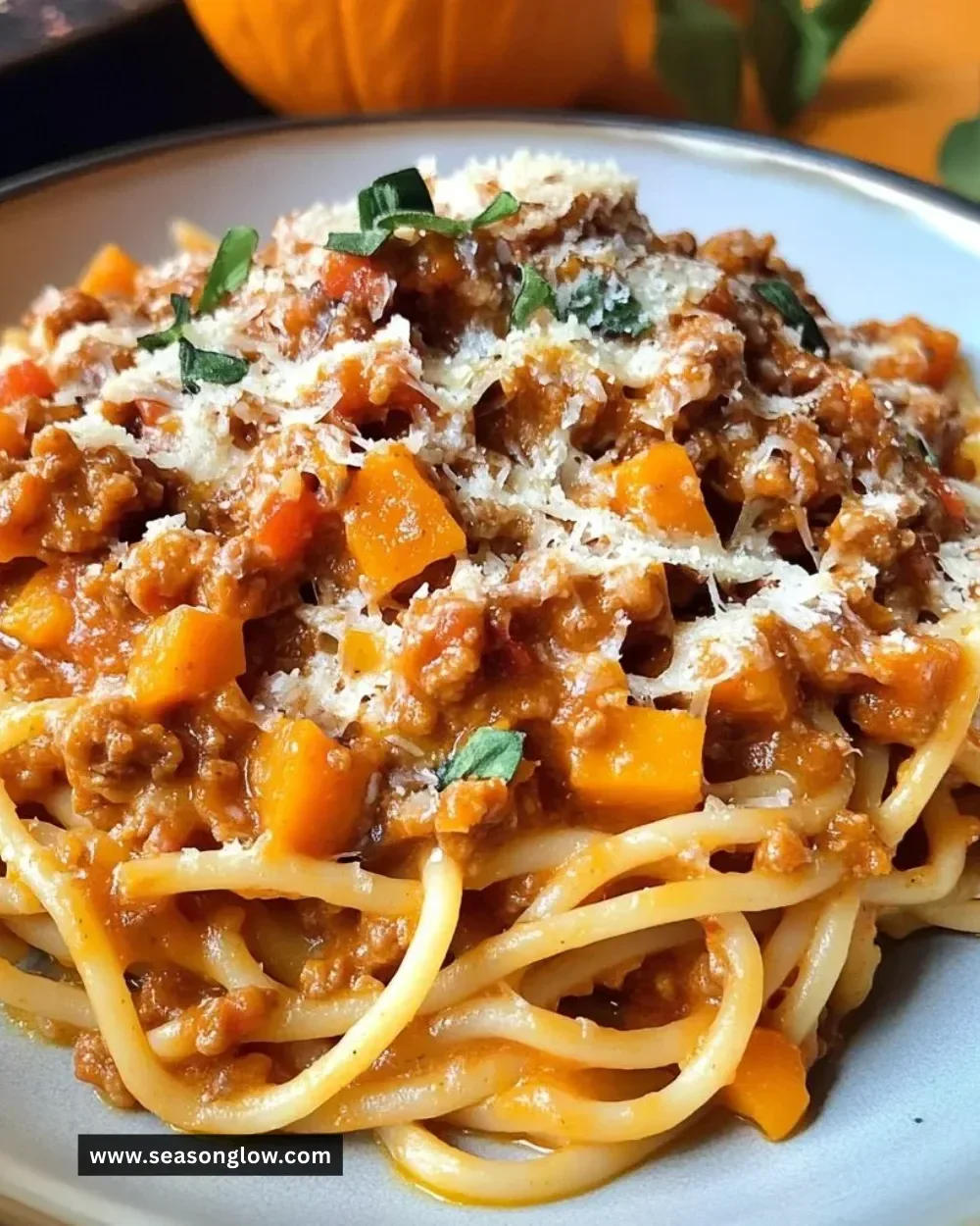 A bowl of Pumpkin Bolognese pasta topped with Parmesan cheese and fresh herbs.
