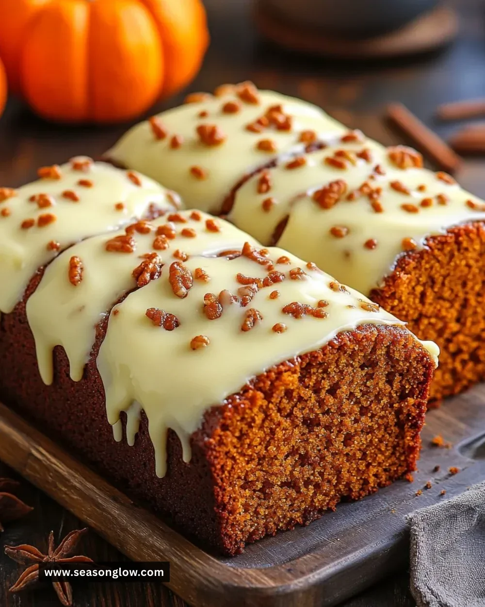 A slice of pumpkin bread topped with smooth cream cheese frosting on a wooden table.
