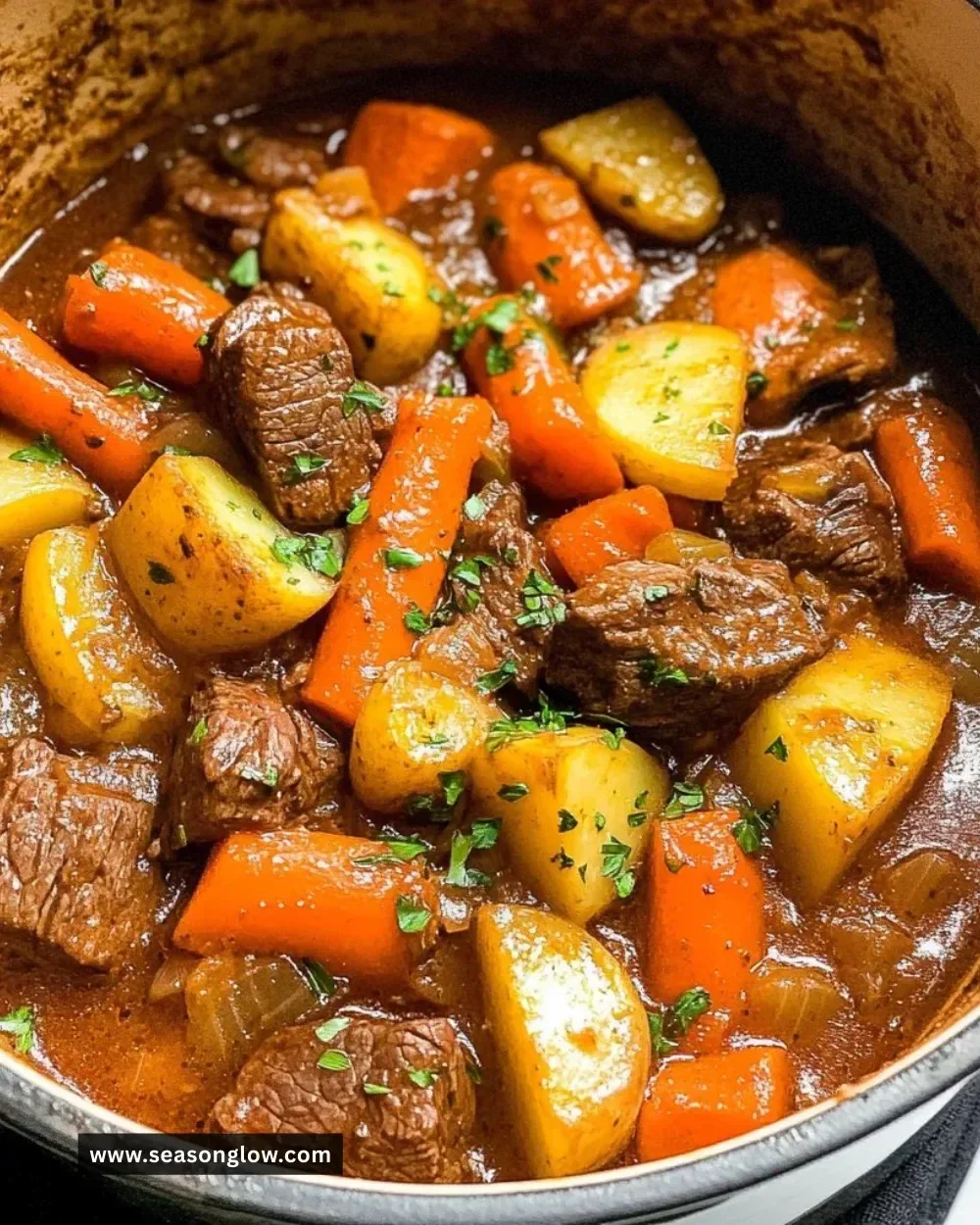 Stove top beef stew simmering in a pot with fresh vegetables and herbs