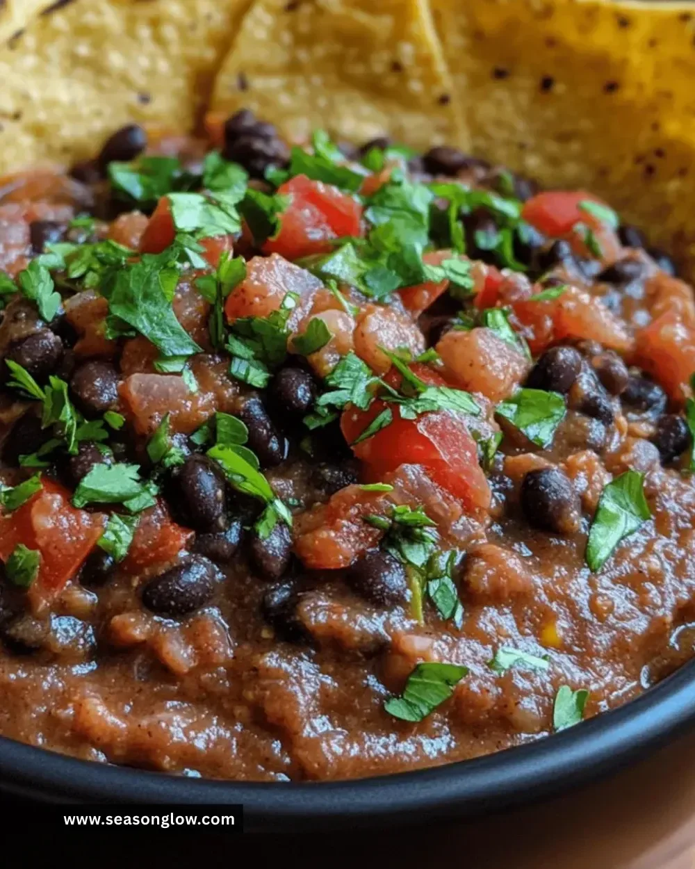 Delicious bowl of spicy black bean dip garnished with cilantro and served with tortilla chips.
