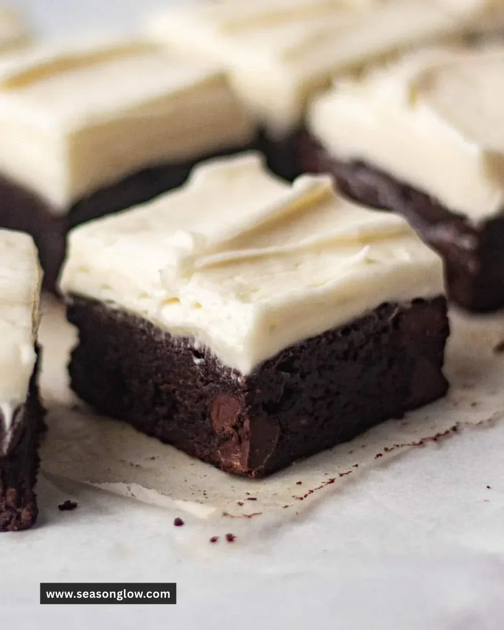 Delicious brownies topped with rich cream cheese frosting on a white plate