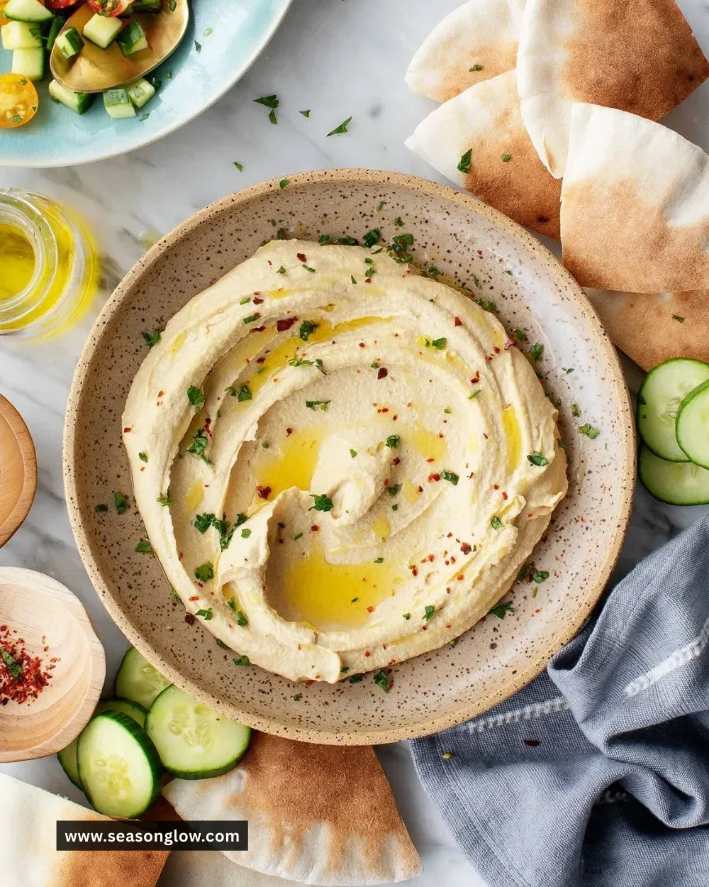 A bowl of creamy hummus garnished with olive oil and fresh herbs.