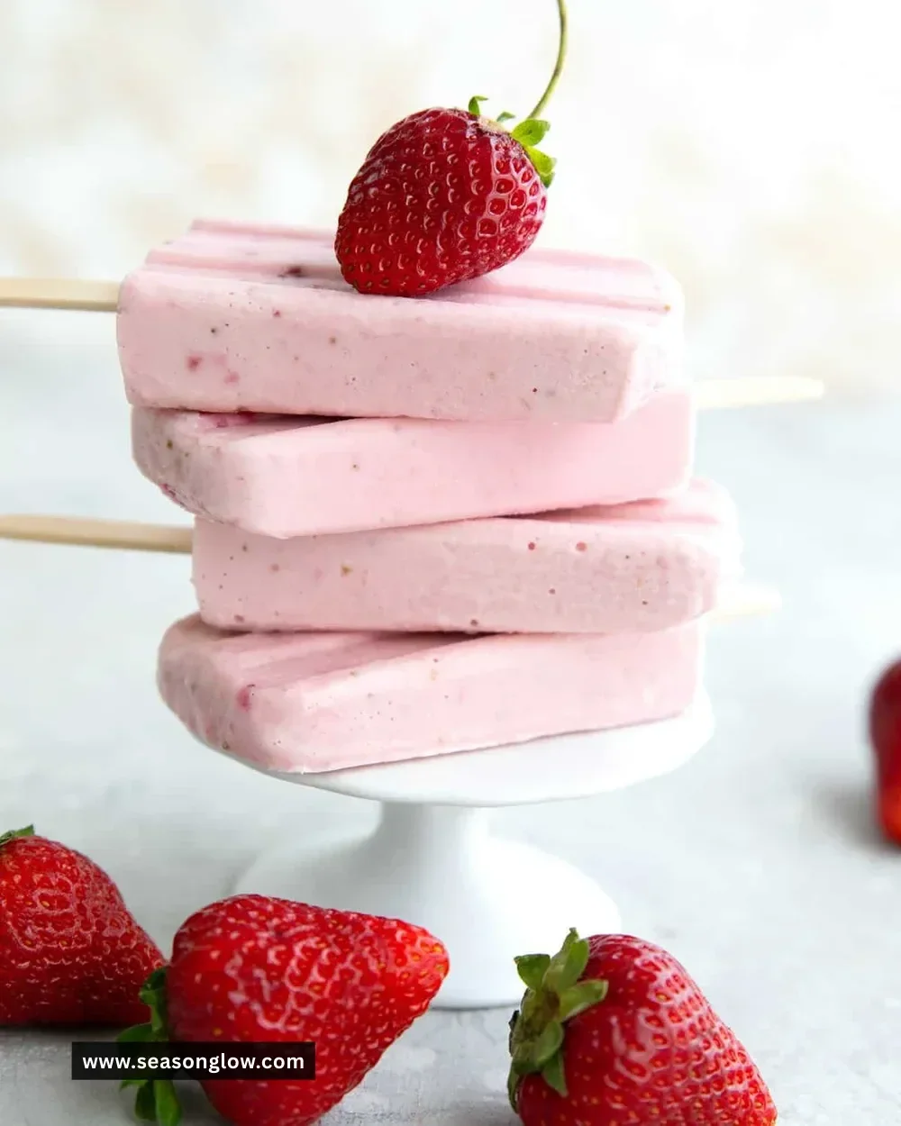 Keto strawberry cheesecake popsicles on a wooden surface with fresh strawberries
