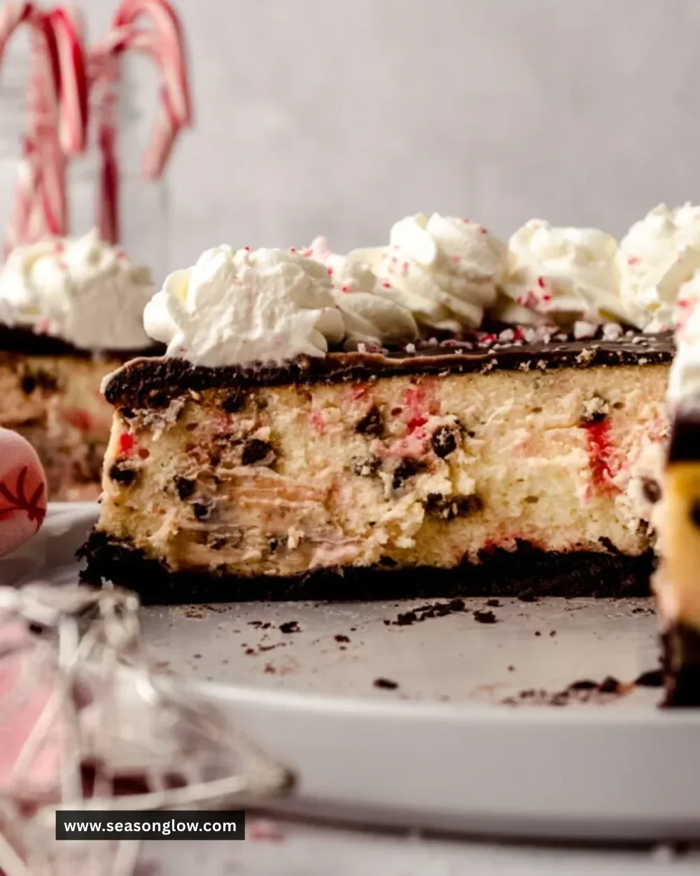 Slice of peppermint bark cheesecake topped with chocolate and crushed peppermint candy.