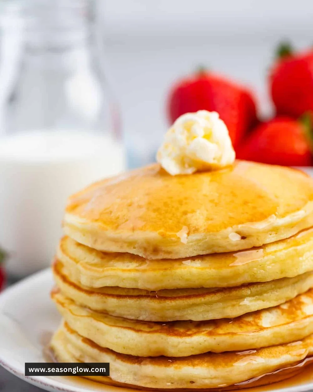 Delicious fluffy pancakes stacked high on a plate with syrup and berries