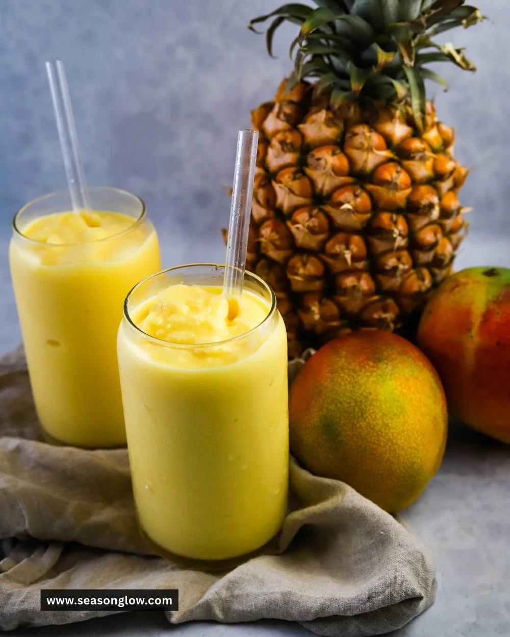 A refreshing Mango Pineapple Slushie in a clear glass with tropical fruits