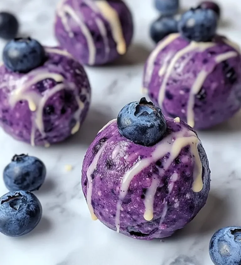 Blueberry cheesecake protein bites stacked on a plate with fresh blueberries.