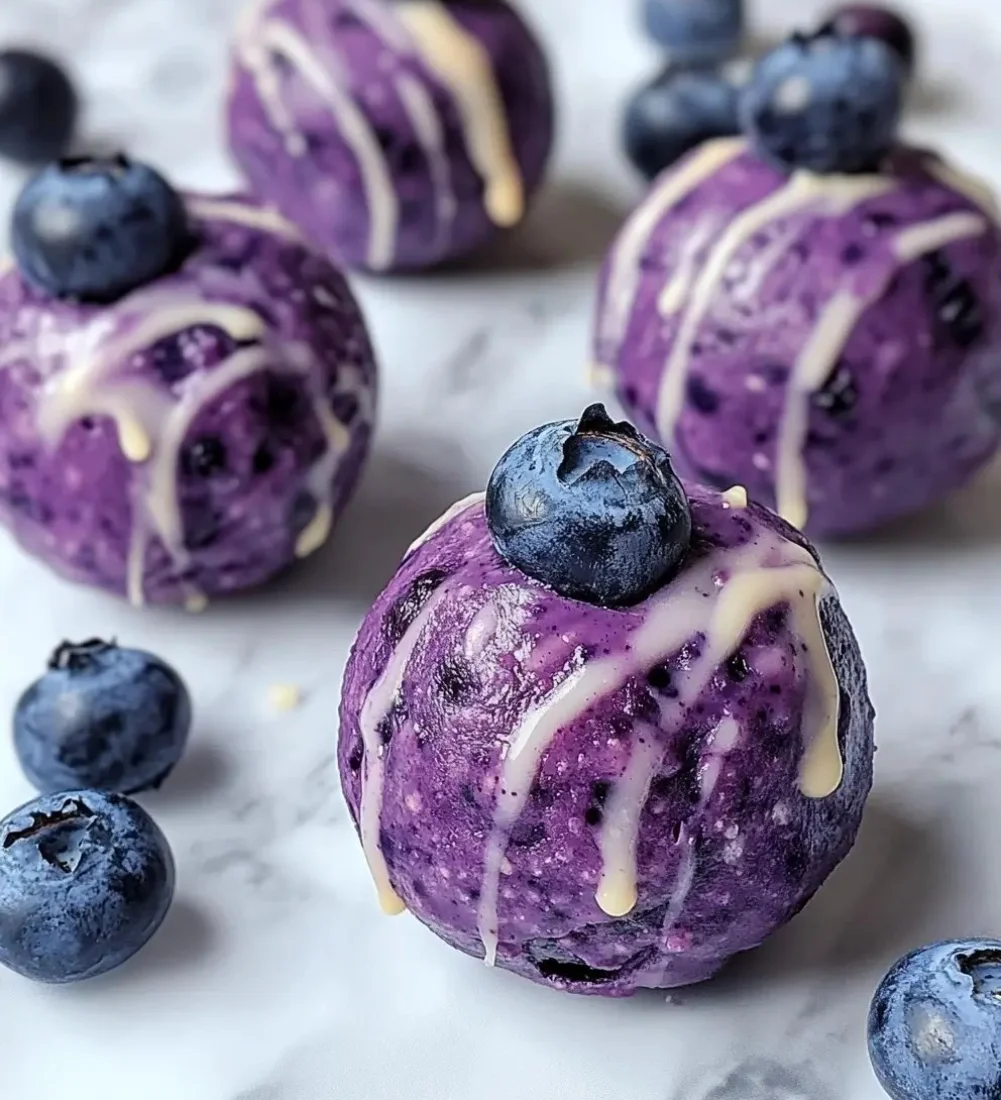 Blueberry cheesecake protein bites stacked on a plate with fresh blueberries.