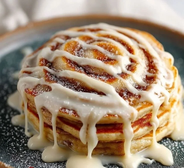 Delicious cinnamon roll pancakes topped with icing and cinnamon swirl.