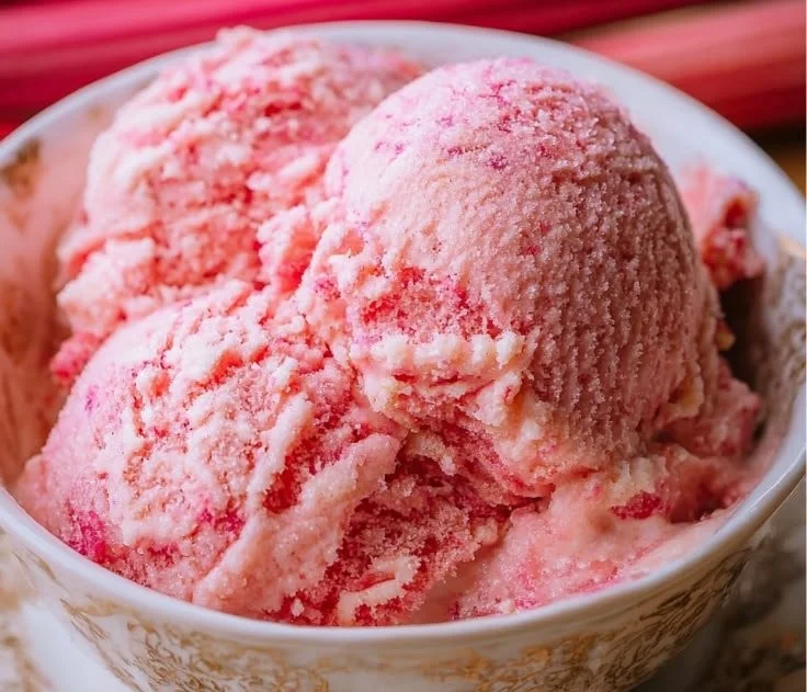 Serving of homemade rhubarb ice cream in a bowl with fresh rhubarb stalks.
